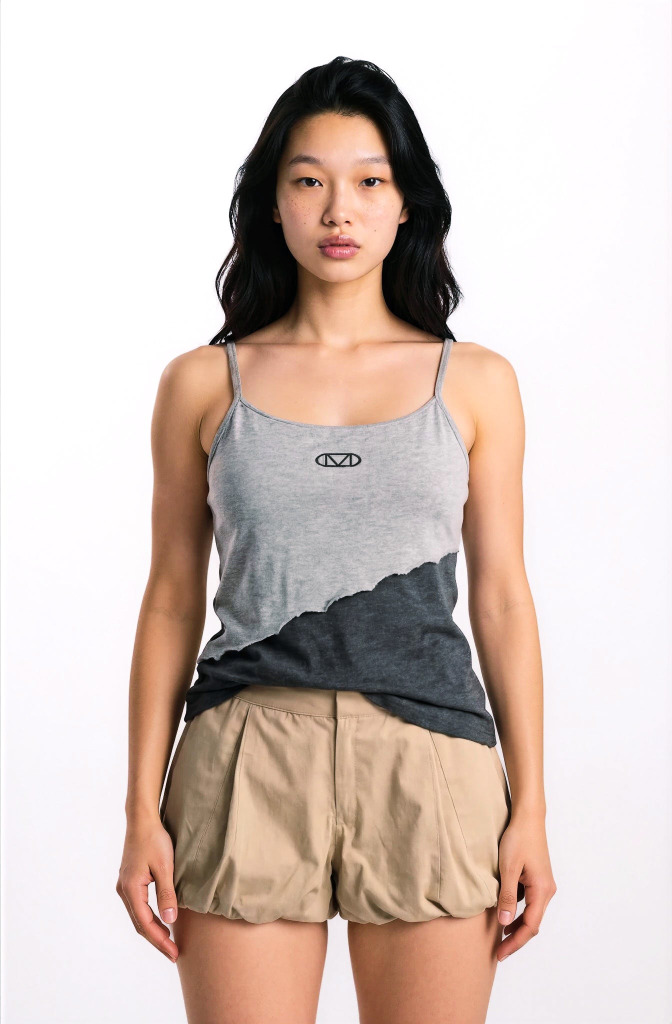 Woman wearing a gray tank top with a logo and beige balloon shorts on a white background
