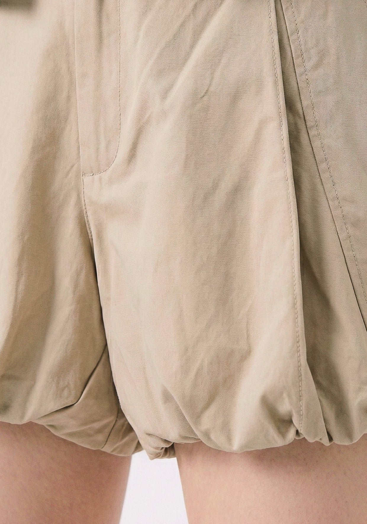 Beige balloon shorts worn with a denim jacket on a plain background